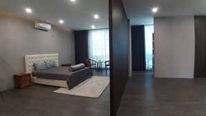 A modern bedroom with a large bed, bedside tables, a desk, and a chair. There is a window with curtains and an air conditioning unit on the wall. - Quy Nhon Hotel (Quy Nhon)