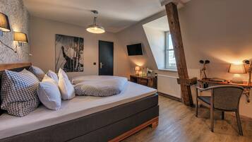 A bedroom with a bed, a desk, a chair, a window, and artwork on the walls.