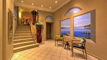 Um saguão de hotel com uma escadaria, uma área de estar com vista para um lago e um relógio na parede.
