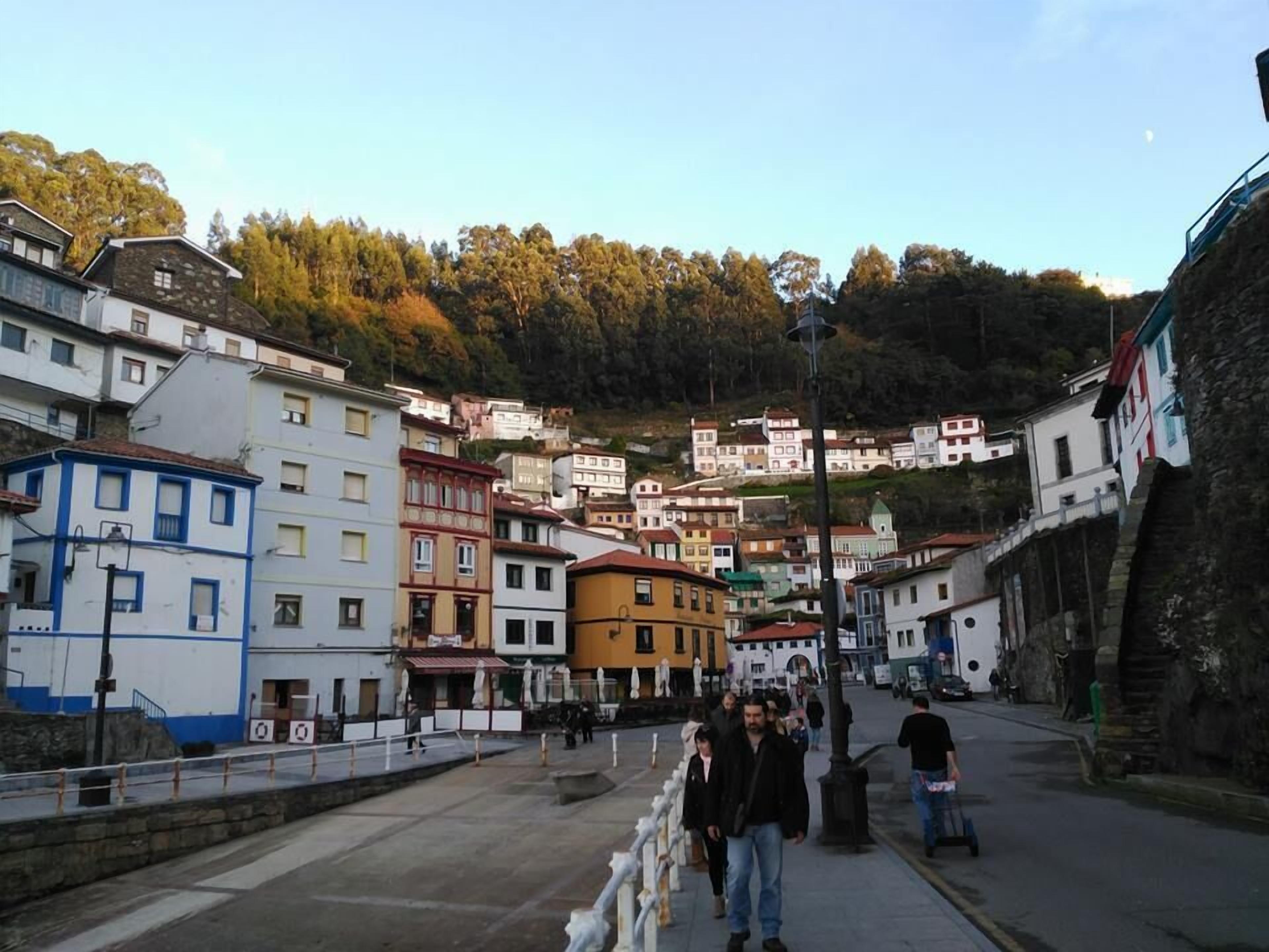 Un pueblo costero con edificios de colores, un paseo marítimo y un telón de fondo montañoso.