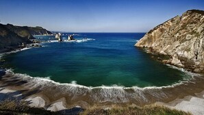 A coastal landscape with a clear view of the sea, rocky cliffs, and a sandy beach. - Apartamentos Rurales La Torre (Valdes)