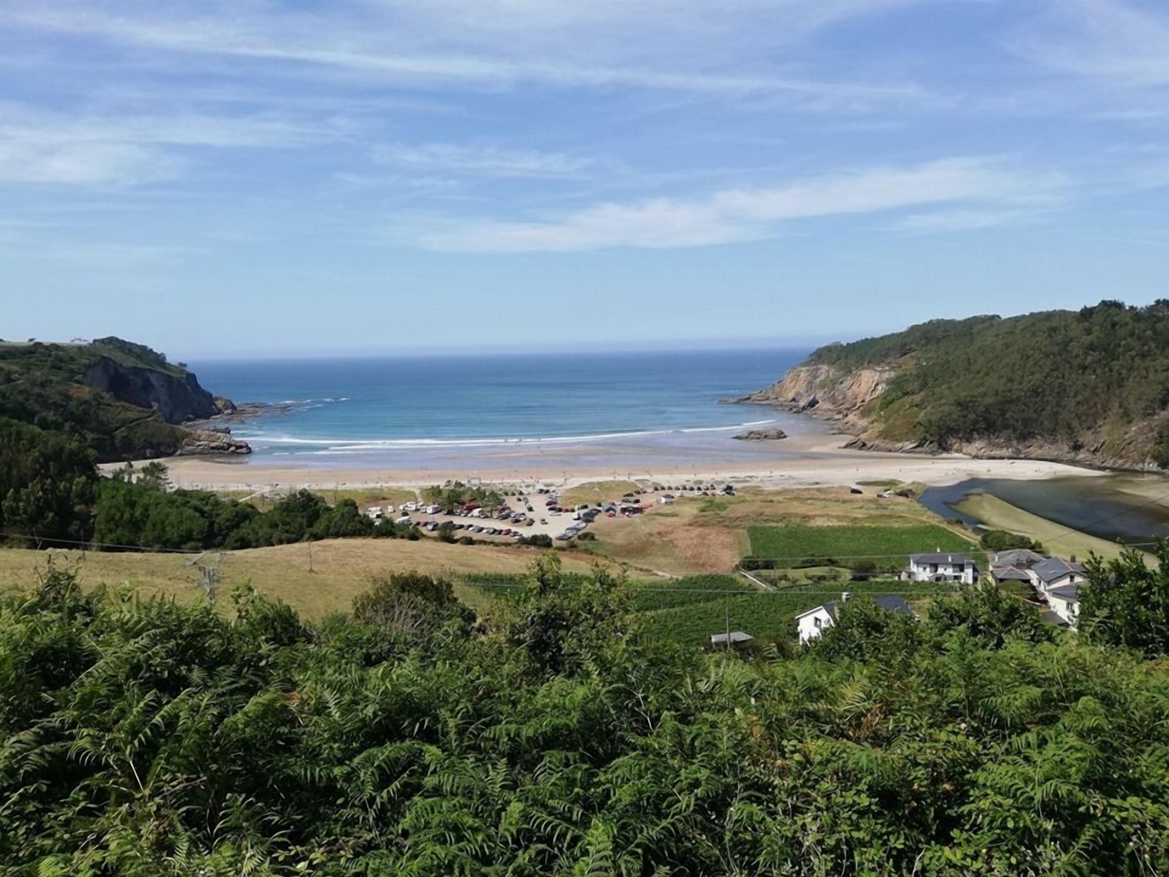 Vista costera con playa, zona de estacionamiento y un pequeño conjunto de edificios.