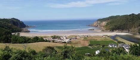 Vista costera con playa, zona de estacionamiento y un pequeño conjunto de edificios.