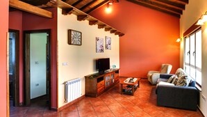 A cozy living room with a wooden ceiling, a sofa, a coffee table, and a television. - Apartamentos Rurales La Torre (Valdes)