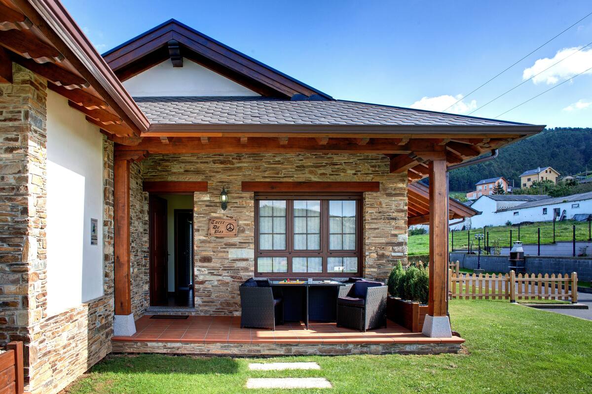 Une maison en pierre dotée d’un patio couvert, d’un coin repas avec des chaises et offrant une vue sur le paysage environnant.