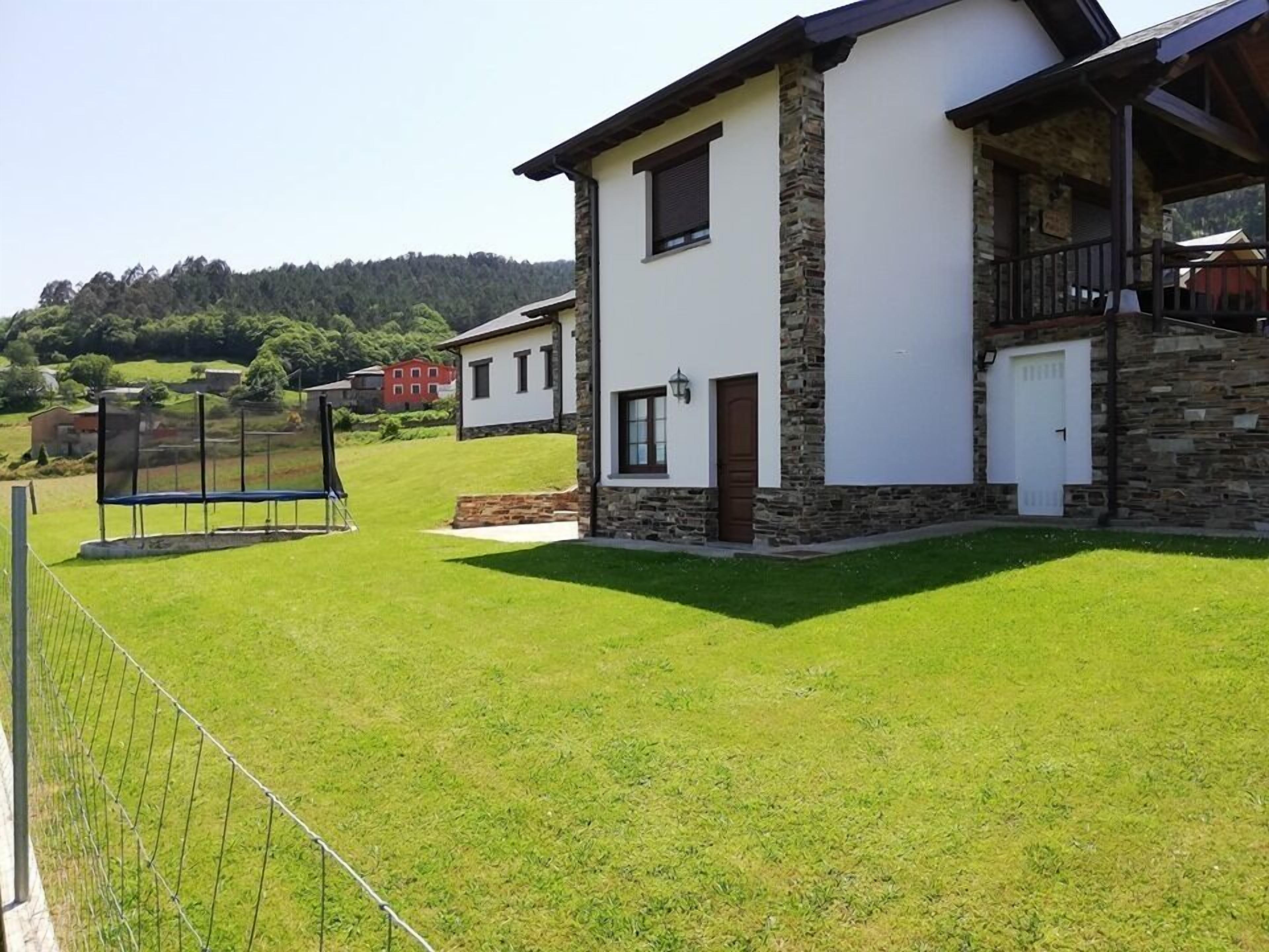 A modern two-story house with a stone facade, a balcony, and a well-maintained lawn.