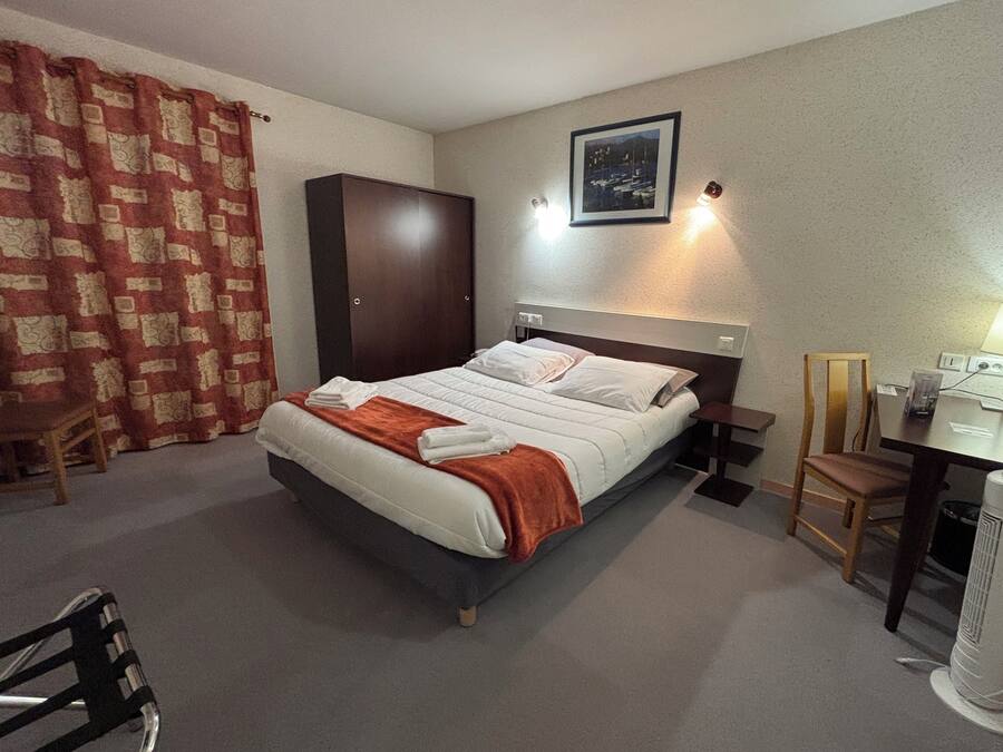A hotel room with a bed, a desk, a chair, a wardrobe, and a picture on the wall.