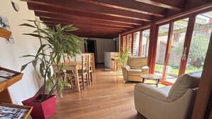 A spacious living room with wooden flooring, a dining area with a wooden table and chairs, a beige sofa, and a large potted plant. - Hôtel les Hirondelles (Orcines)