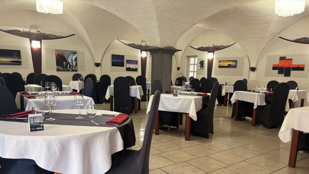 A restaurant with multiple tables, black chairs, and white tablecloths. - Hôtel les Hirondelles (Orcines)
