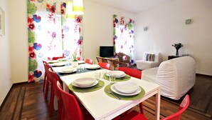 Un coin repas avec une table dressée pour quatre personnes, des chaises rouges, un téléviseur et un canapé recouvert d’une housse.