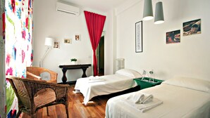 Une chambre d’hôtel avec deux lits simples, une chaise en osier, un bureau avec une lampe et un rideau rouge.