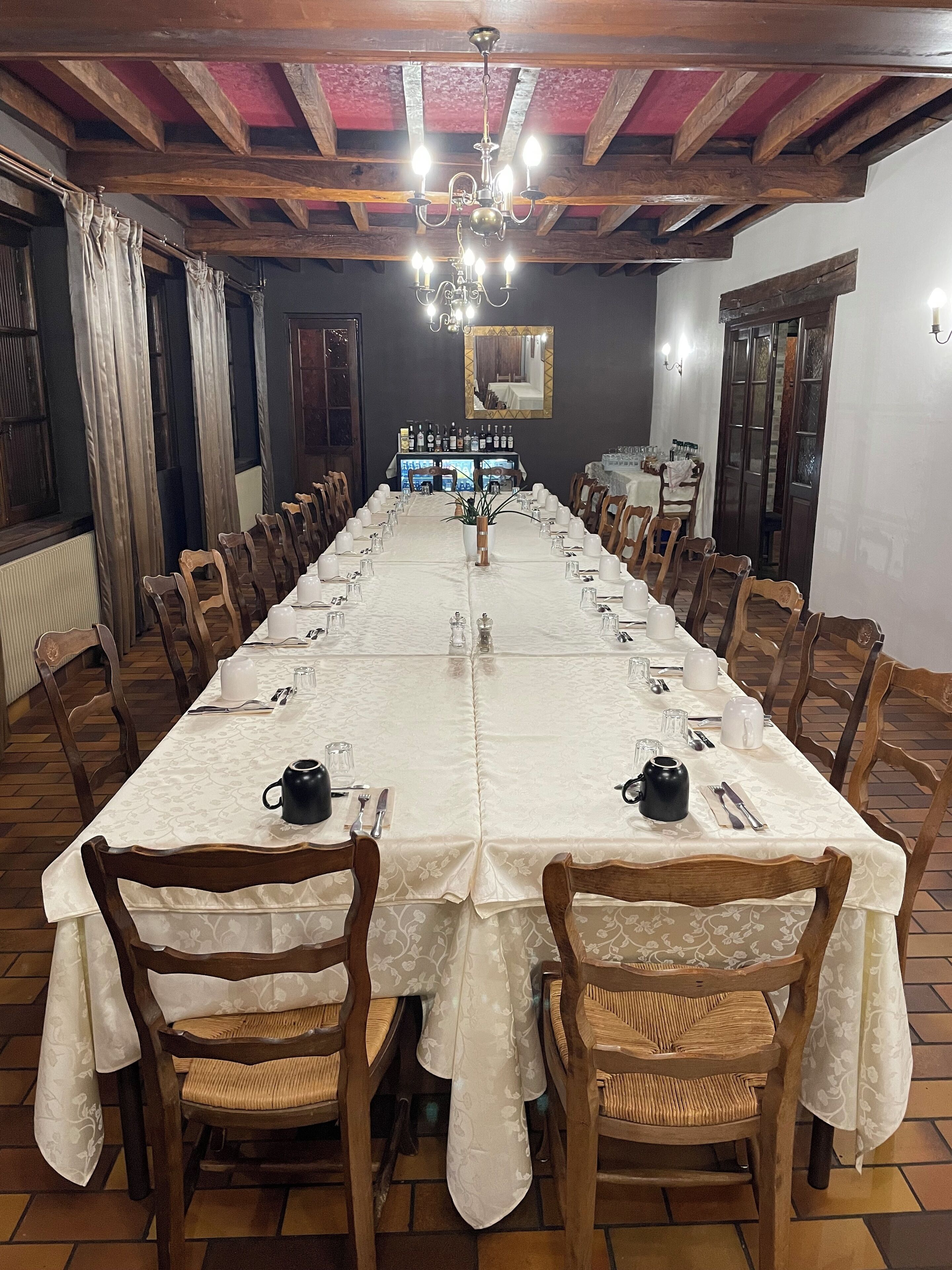 A long dining table with white tablecloths, wooden chairs, and a chandelier.