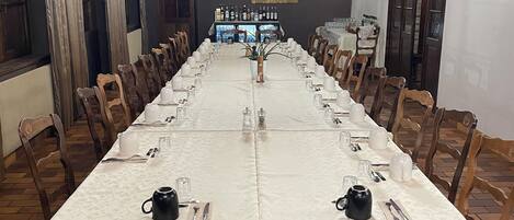 A long dining table with white tablecloths, wooden chairs, and a chandelier.