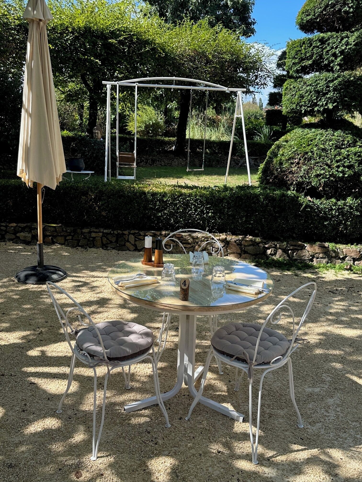 Un patio jardín con una mesa redonda de cristal, cuatro sillas acolchadas, un columpio y una pérgola.