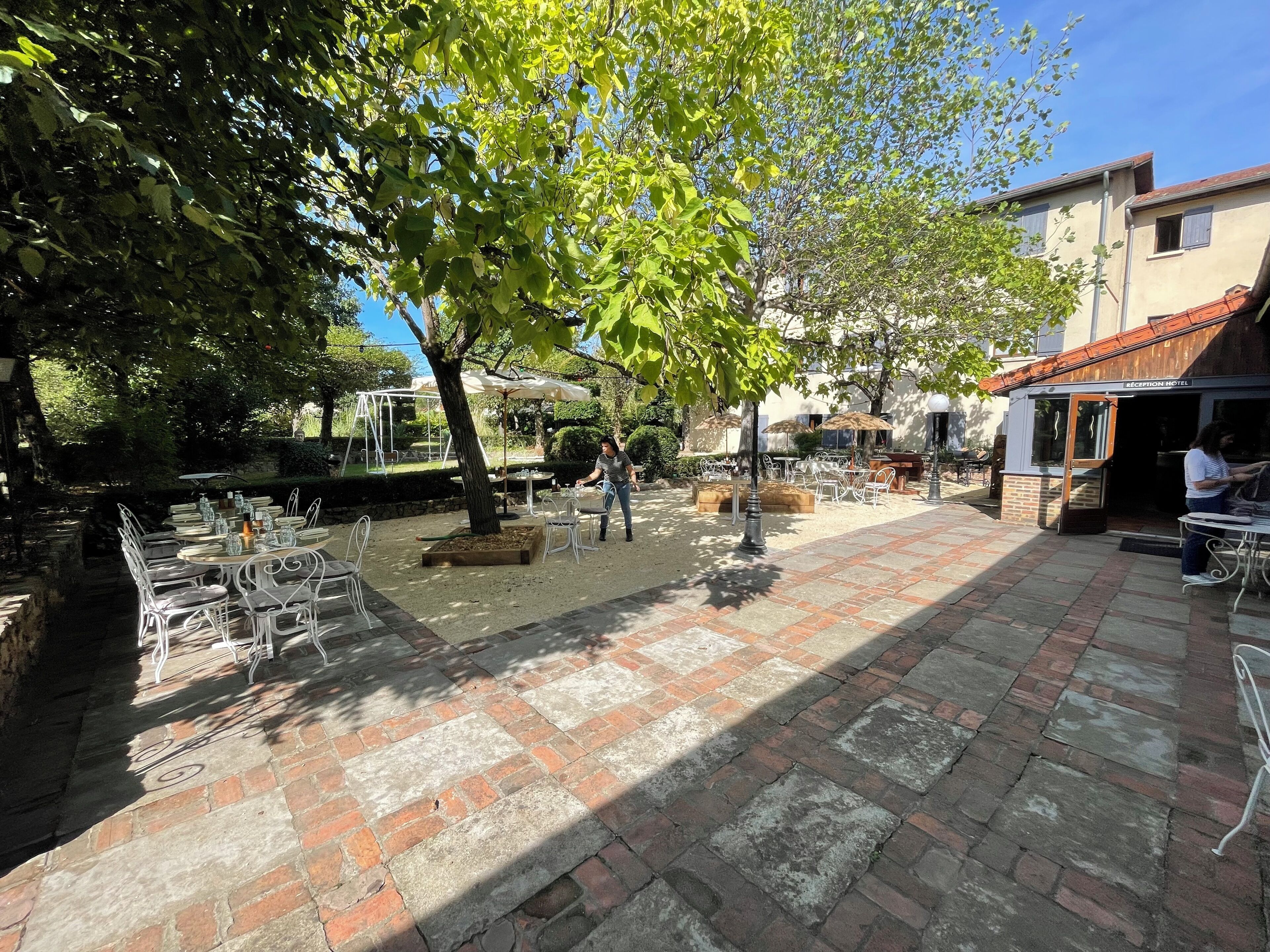 An outdoor patio with tables and chairs, a reception area, and a building labeled "RECEPTION HOTEL" in the background.