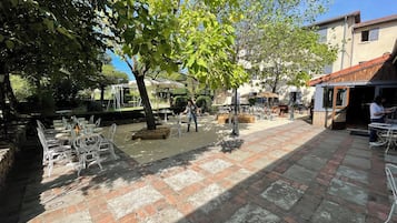 Un patio exterior con mesas y sillas, una zona de recepción y un edificio con el rótulo "RECEPTION HOTEL" al fondo.