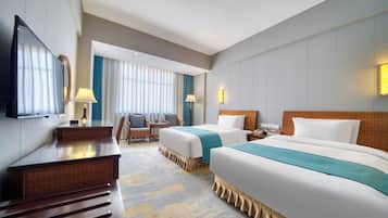 Quarto de hotel com duas camas, uma escrivaninha, uma cadeira, uma televisão e um abajur.
