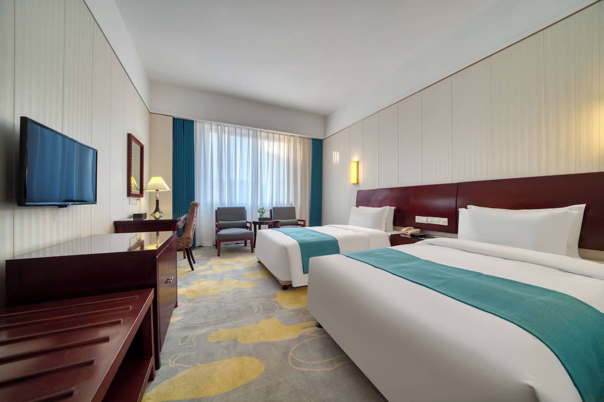Habitación de hotel con dos camas, un escritorio, una silla, un televisor y una ventana con cortinas.