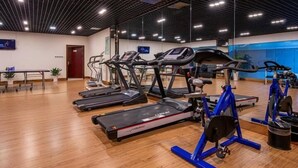 Un gimnasio con cintas de correr, bicicletas estáticas y un espejo grande.