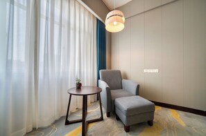 A hotel room with a grey armchair, a small round table with a plant, and a hanging light fixture. - Haiwaihai International Hotel  (Hangzhou)
