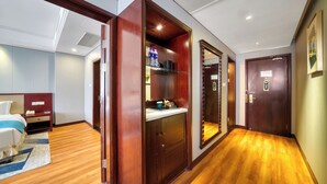 Habitación de hotel con piso de madera, una cama con cabecera azul, un escritorio con silla y un armario.