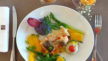 A plate of food with various vegetables and a piece of fish, accompanied by a glass of wine and a vase with a yellow rose.