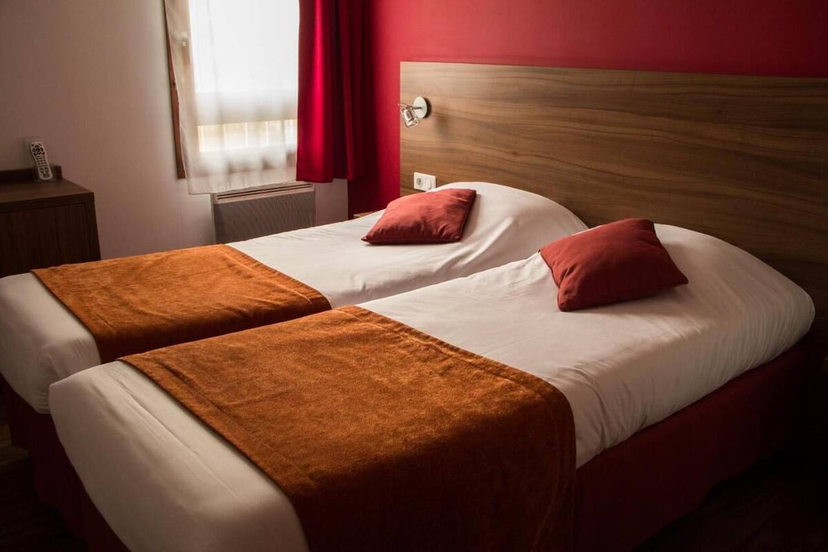 Een tweepersoonsbed met een houten hoofdeinde, twee kussens en een bruine plaid.