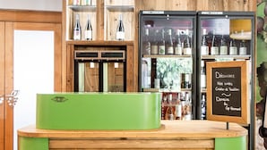 Een receptiegedeelte met een houten balie en groene accenten, een glazen vitrine met flessen, en een menukaart op een schoolbord.