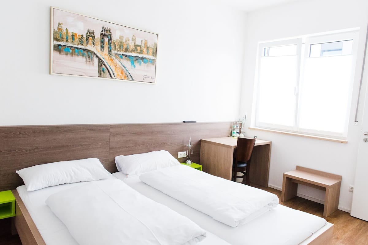 A hotel room with two beds, a desk, a chair, a small table, and a painting on the wall.