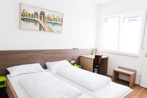 Quarto de hotel com duas camas, uma escrivaninha, uma cadeira, uma mesinha e um quadro na parede.