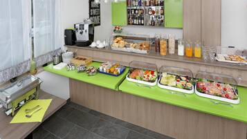 Buffet montado com diversos alimentos e bebidas, uma máquina de café e um balcão verde.