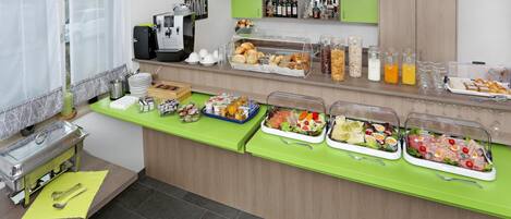 Montaje de bufé con diferentes alimentos y bebidas, una máquina de café y una barra verde.