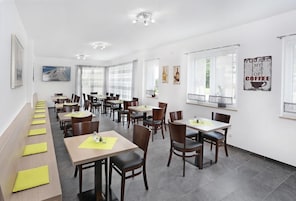 Uma sala de jantar moderna com várias mesas e cadeiras, um longo banco com jogos americanos amarelos, e uma parede com um letreiro com tema de café.