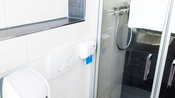 Ein modernes Badezimmer mit Toilette, einem Händetrockner, einer Duschkabine aus Glas und einem Waschbecken.