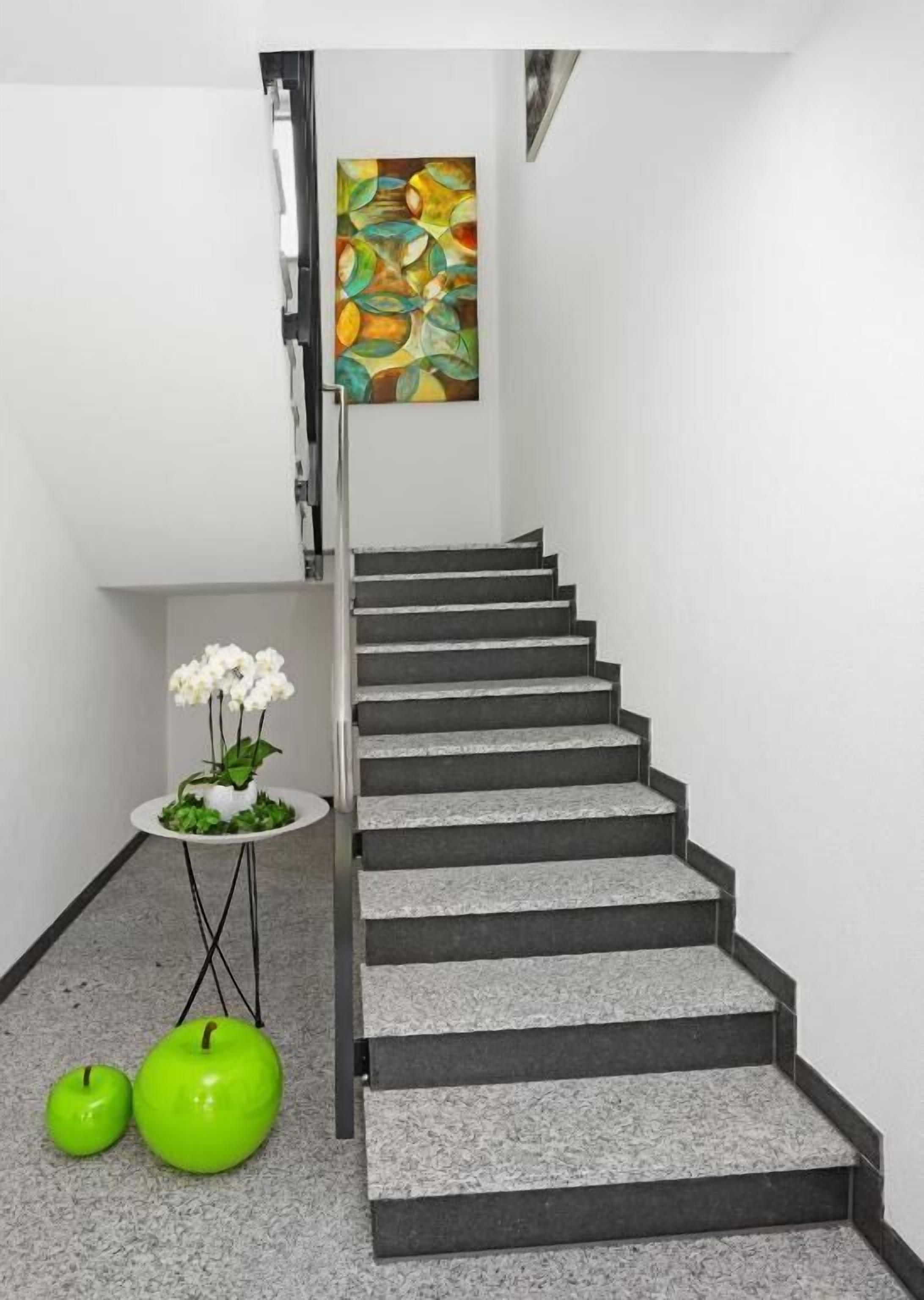 A staircase with a modern design, a small table with a potted plant, and two green apples on the floor.