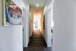 Um corredor com paredes brancas, soalho de madeira escura e quadros enquadrados nas paredes.
