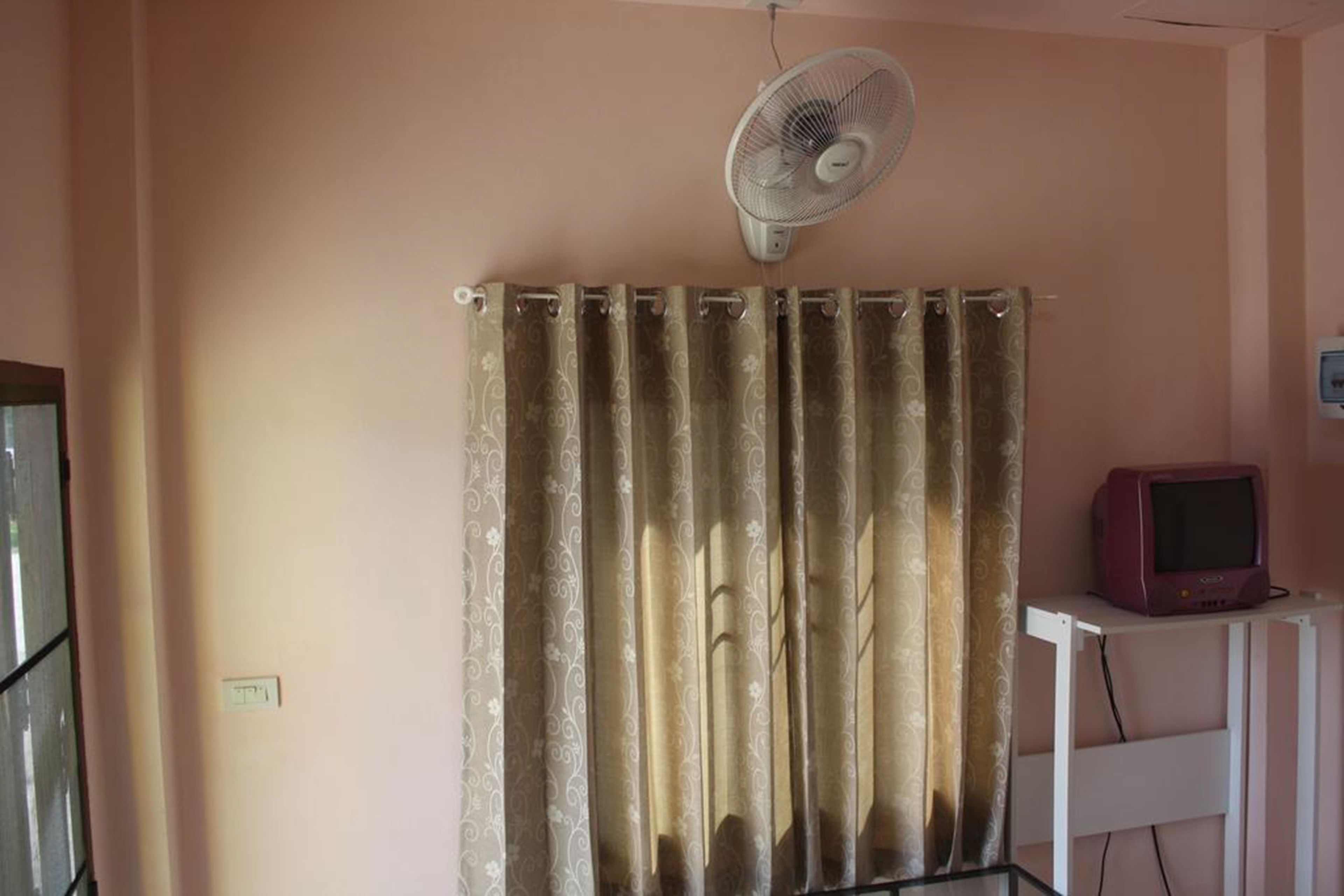 A room with a curtain, a standing fan, and a television on a stand.