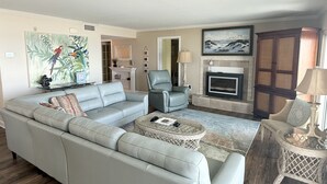 A modern living room with a sectional sofa, a glass coffee table, a fireplace, and a painting of birds.