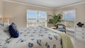 A bedroom with a large bed, a chair, a plant, and a view of the beach.