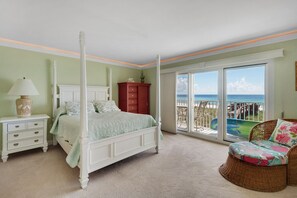 A bedroom with a four-poster bed, a nightstand with drawers, a red dresser, and a wicker chair with a floral cushion.