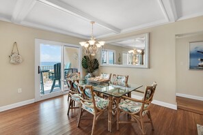 A dining area with a glass table and wicker chairs, a chandelier, and a large mirror on the wall.