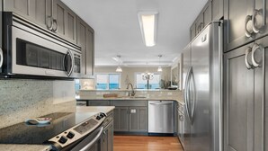 A modern kitchen with stainless steel appliances, granite countertops, and wooden flooring.
