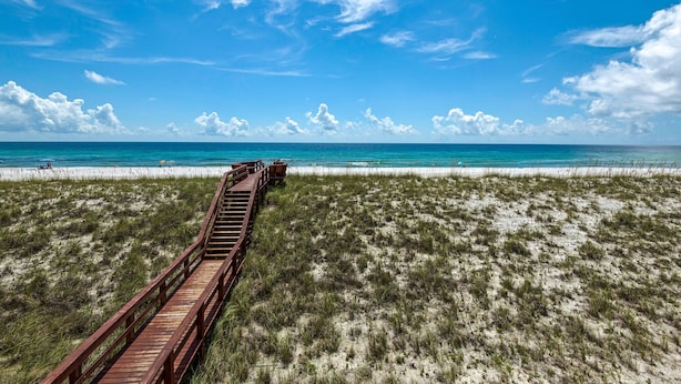A wooden boardwalk leading to a beach with clear blue water and white sand.