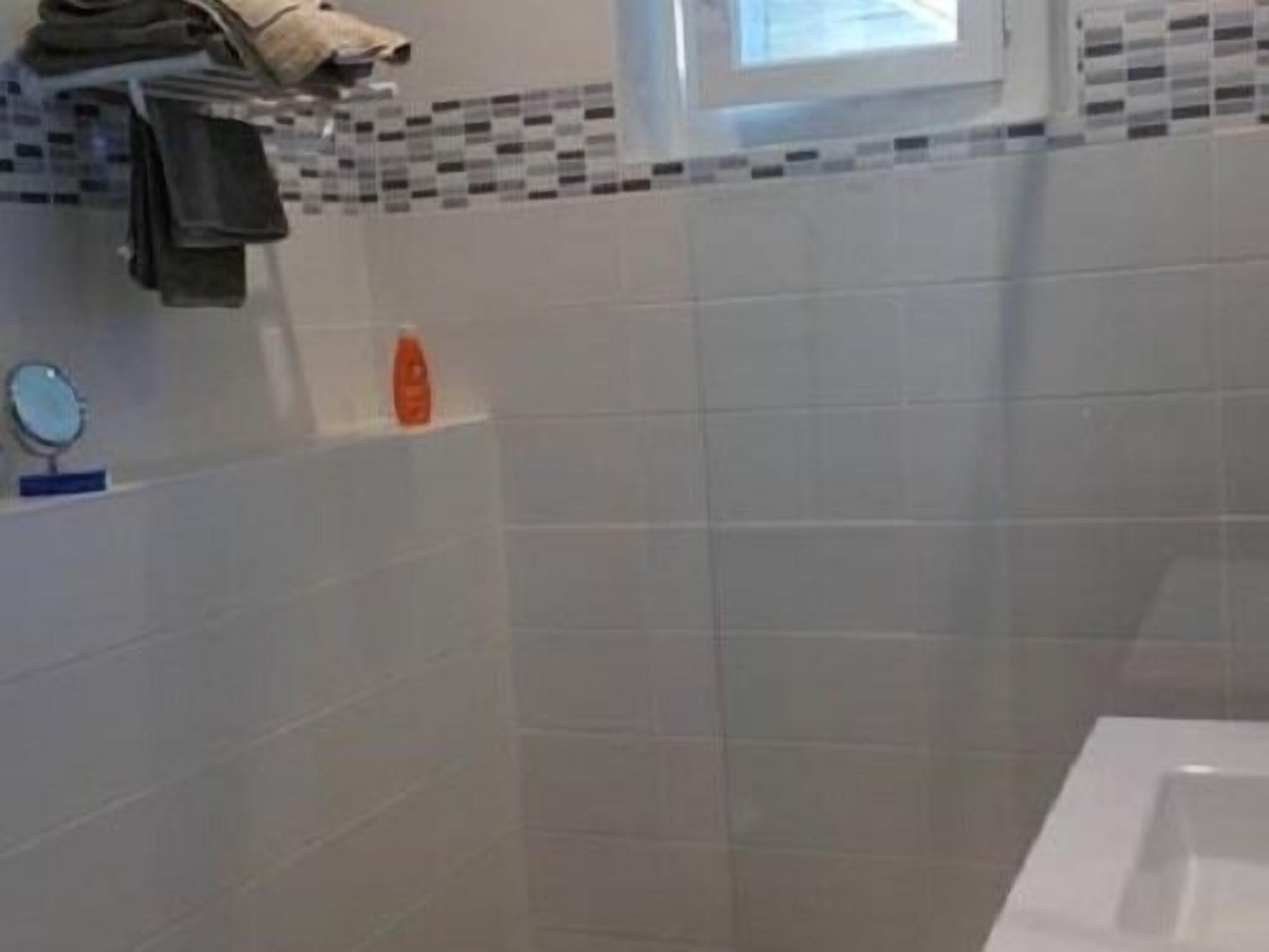 A bathroom with a white bathtub, a small shelf with toiletries, and a window above the sink.