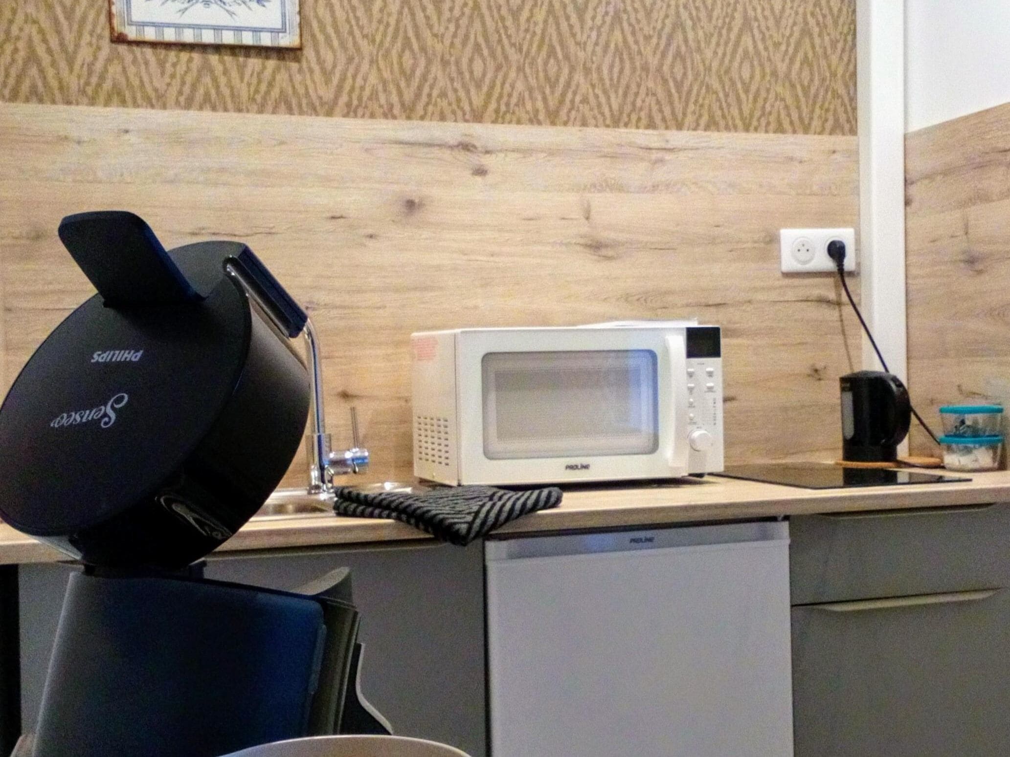 Une cuisine équipée d’un four à micro-ondes, d’une bouilloire et d’un haut-parleur noir posé sur un plan de travail en bois.