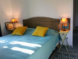 Una cama con una colcha azul y dos almohadas amarillas, con dos mesitas de noche a ambos lados y lámparas.