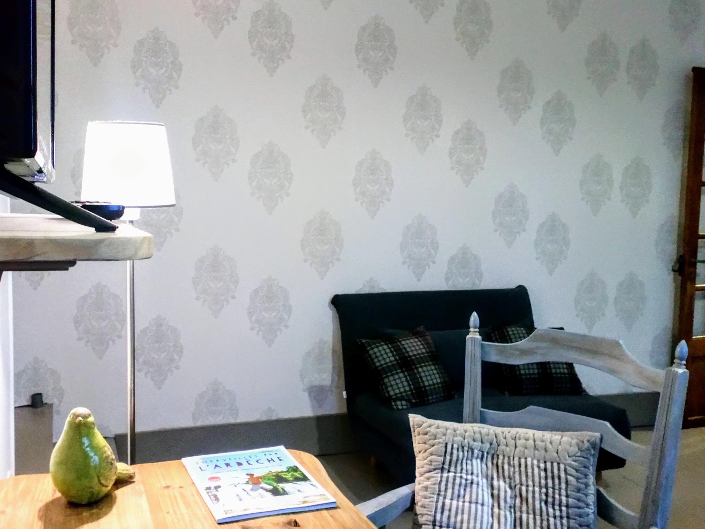 A cozy living room with a dark green sofa, a white armchair, a wooden side table with a book, and a small green figurine.