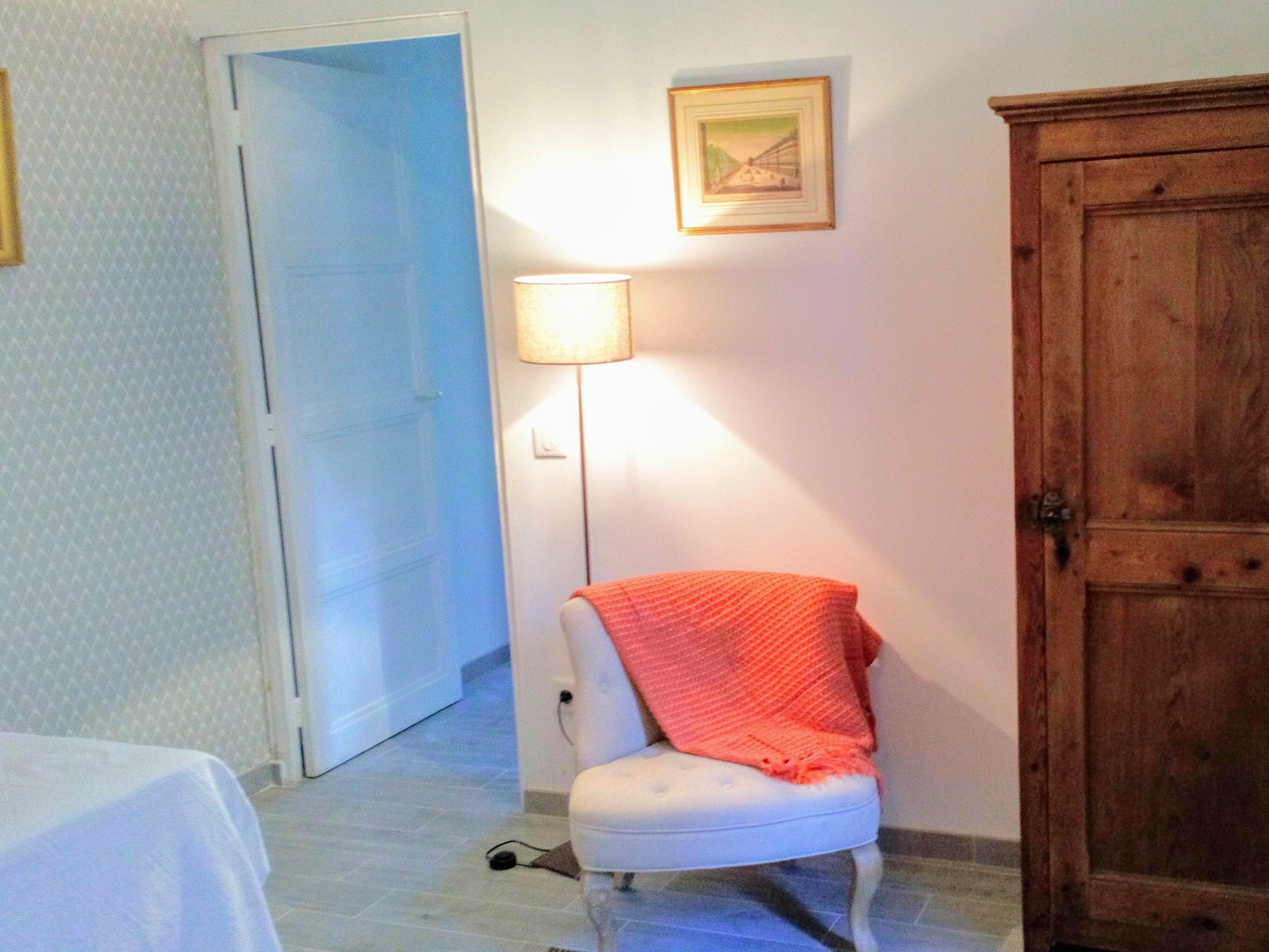 A room with a white chair, a wooden wardrobe, a lamp, and a door.