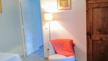 A room with a white chair, a wooden wardrobe, a lamp, and a door.