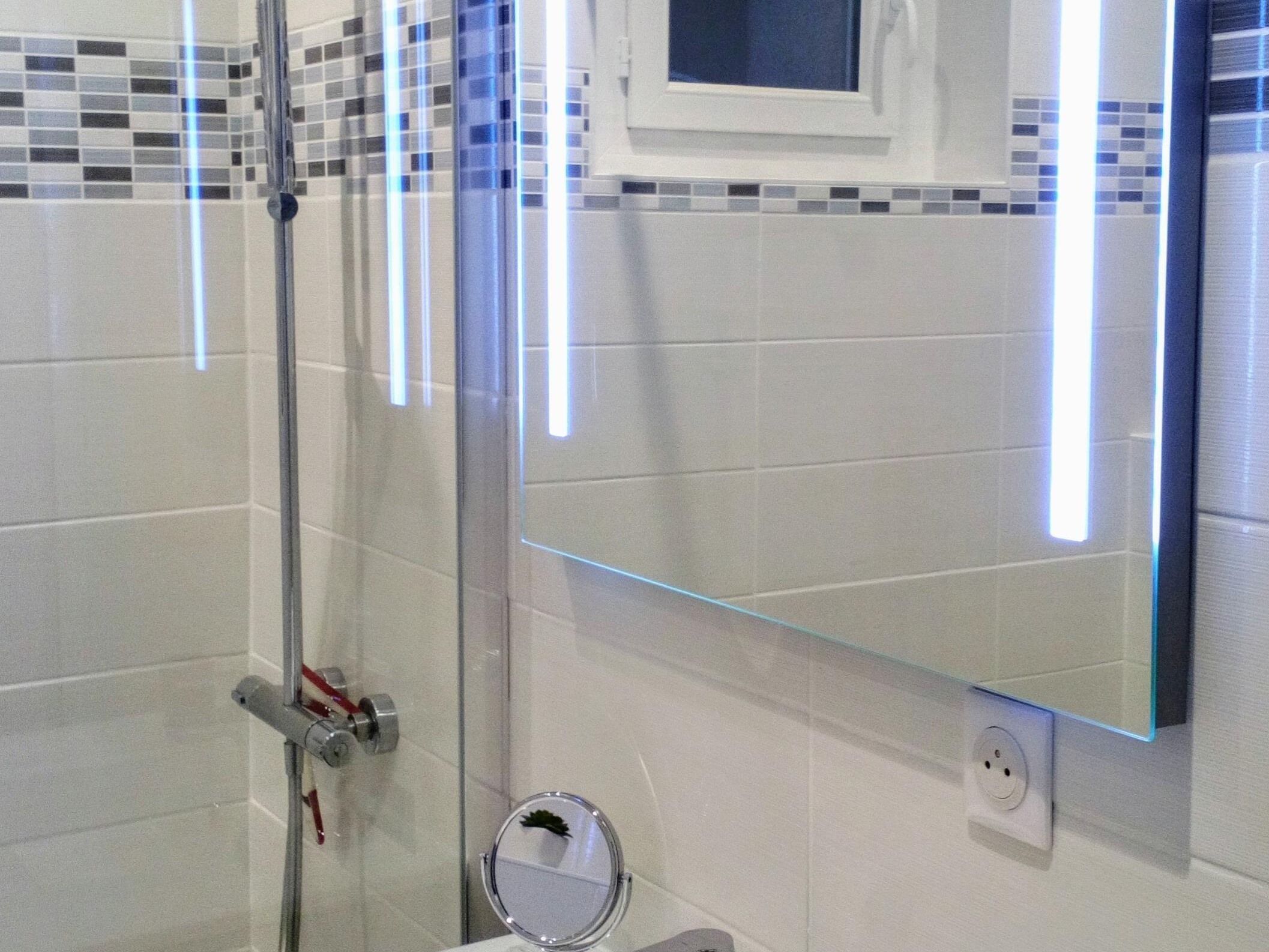 Un baño moderno con cabina de ducha de vidrio, un espejo instalado en la pared y una pequeña ventana sobre el espejo.